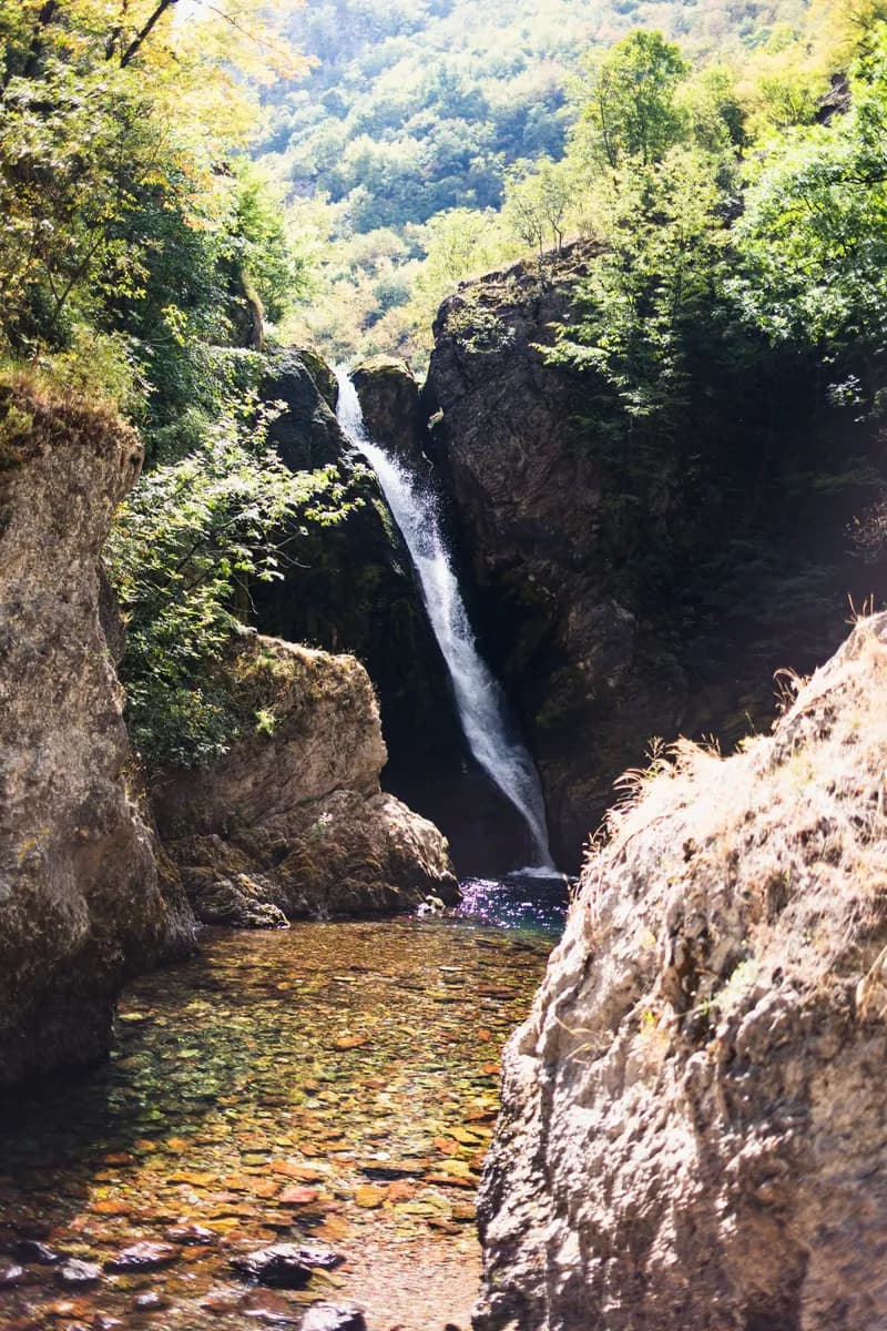 A slender waterfall dropping into a pool between rocks and greenery.