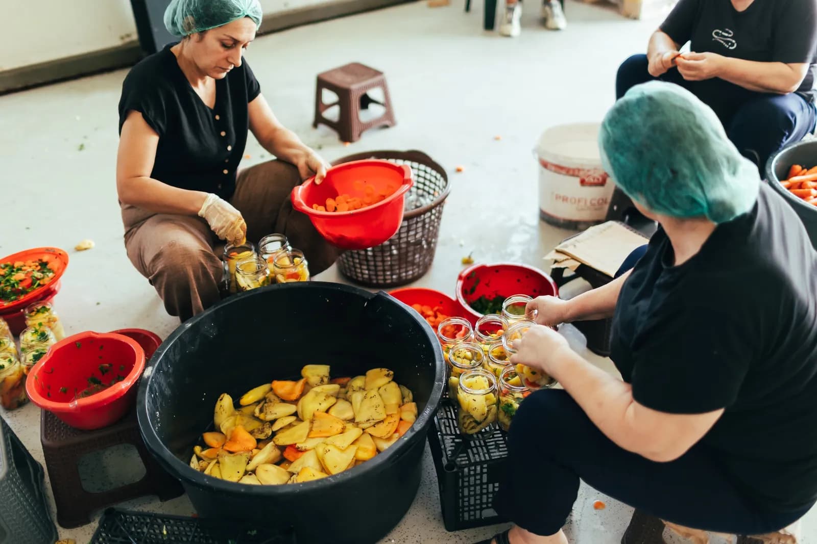 Women in hairnets cutting and sorting peppers in a workshop.