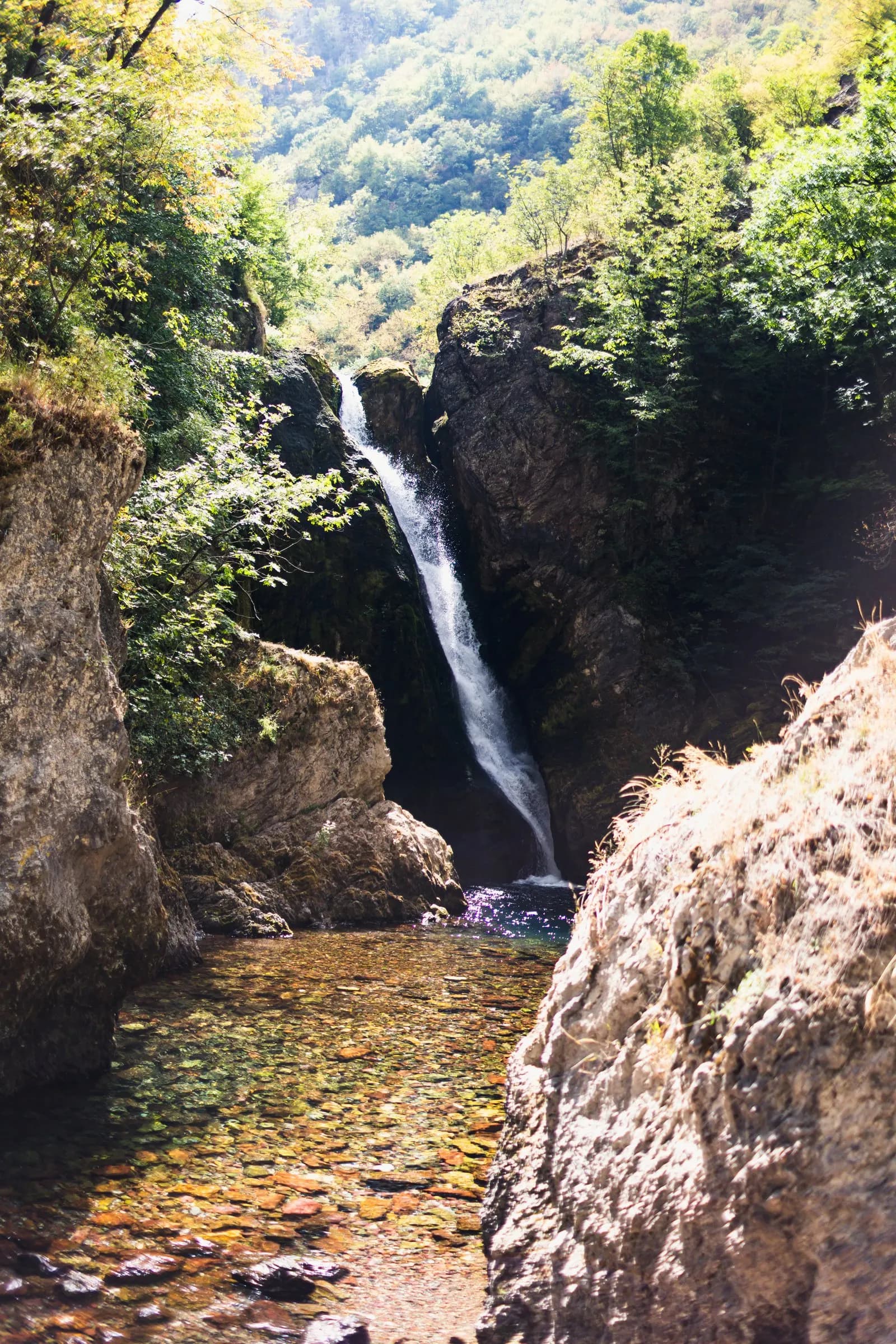 A slender waterfall dropping into a pool between rocks and greenery.