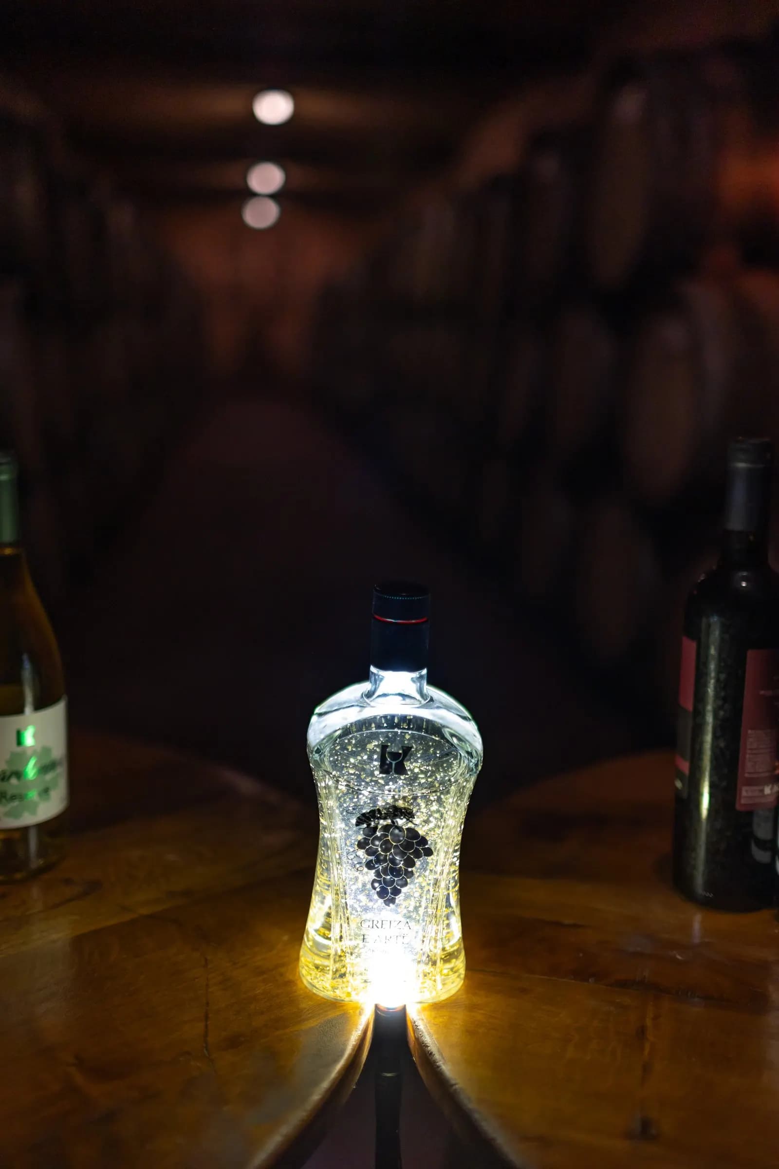 A glass bottle lit from within, standing on a wooden barrel in a dim cellar.
